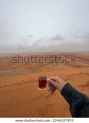 Picture of a hand holding a cup of tea in middle of the desert