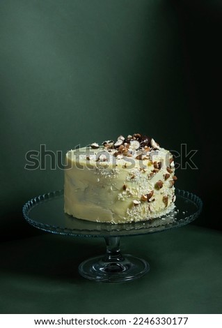 Festive banana cake in white chocolate,decorated with nuts, cookies and chocolate on a dark green background. exclusive pastries according to the author's recipes.for a culinary blog and a pastry shop