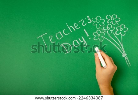 The teacher's hand writes on the blackboard. Chalk lettering TEACHER'S DAY and a bouquet of flowers on a green blackboard. Concept Teacher's Day.