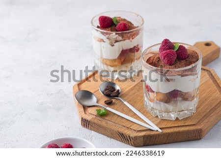 Dessert, tiramisu with raspberries in portion glass glasses on a wooden board on a light concrete background. Italian Cuisine. Valentine's day concept