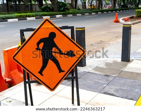 An orange construction traffic sign placed on a sidewalk during empty traffic.
