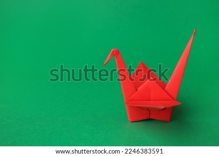 Red paper origami crane on green background, space for text