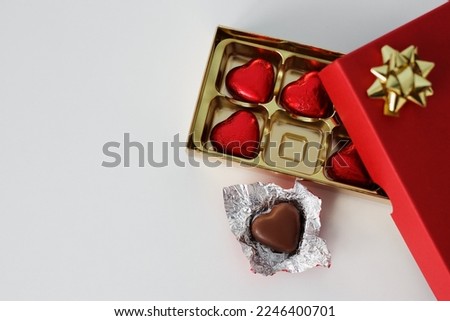 close up of gift box of heart shape chocolate candies in red foil and copy space over white background