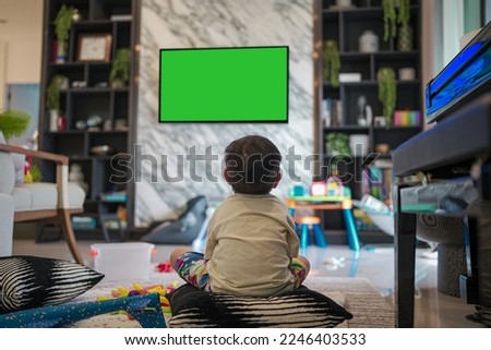 Asian Little kid watching green-screen TV  Alone in the living room, surrounded by a lot of toys.
selective focus, white shirt kids watch media. Back-view.