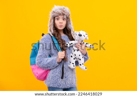 funny kid long hair in hat with schoolbag and toy on yellow background, back to school