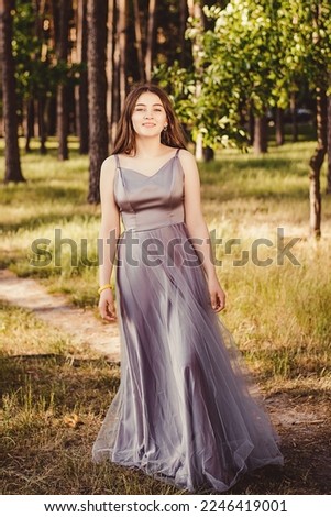 This photo shows a Photo of a gentle cute girl in a gray puffy dress walking in a natural park, outdoor garden and smiling.