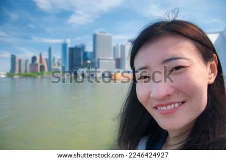 a smiling chinese woman with a blurred new york city background on a sunny day. 