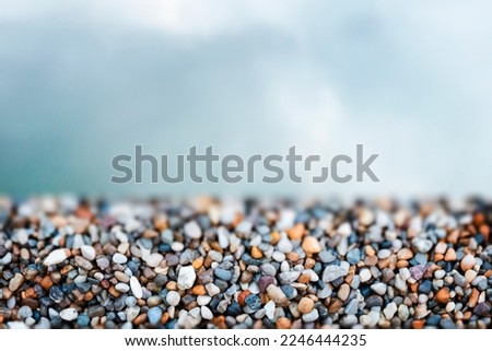 Close-up of small colored beach rocks in the foreground and a blurred sky in the background. Copy space