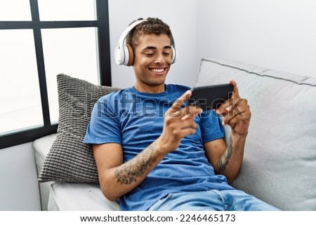 Young hispanic man sitting on the sofa watching video on smartphone at home Royalty-Free Stock Photo #2246465173