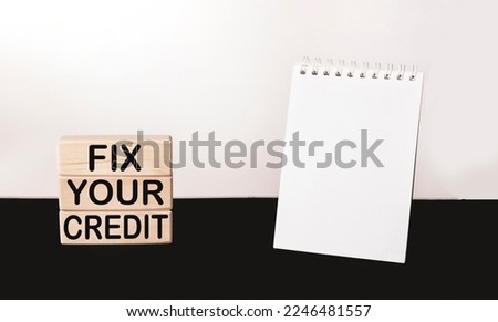Fix Your Credit text written on building blocks and white and black background, next to a notepad for writing.Conceptual photo. Evaluation tips fix improvement