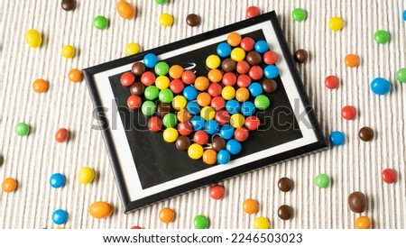 A playful and fun design with small dragee candies arranged like a heart-shaped picture in a frame on a white table.