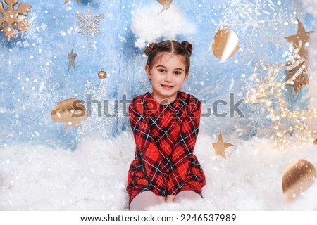 Little girl in dress in the winter forest. Winter wonderland setup with snow, stars and Christmas deer props. 
