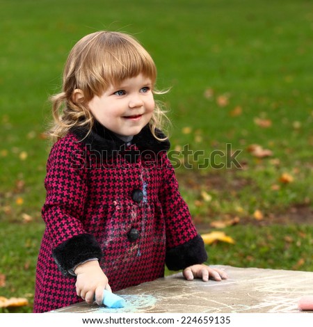 Little girl draws colored chalk on natural background outdoor