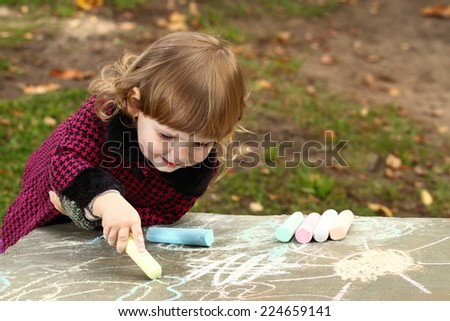 Little girl draws colored chalk on natural background outdoor