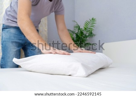 A man tucks a pillow with a fresh bright white pillowcase. Making the bed with fresh bed linen by a white man. The day of the change of bed linen. The day of washing bed linen in the laundry room. Royalty-Free Stock Photo #2246592145