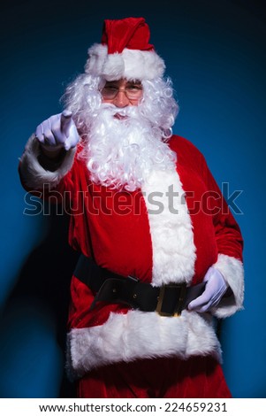 Picture of a Santa Claus pointing at the camera, against blue background.