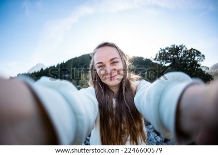 Young woman with blond hair taking a selfie portrait while hiking in the mountains - Happy hiker on top of a cliff smiling at camera - Travel and hobby concept