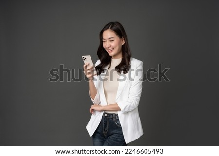Female executive in white suit with long hair, white skin, taking photo in studio against gray background looking at cell phone His face was smiling, excited and hopeful