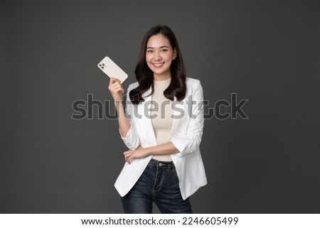 Female executive in white suit with long hair, white skin, taking photo in studio against gray background stand with mobile phone She was standing smiling, her face was beautiful and cute