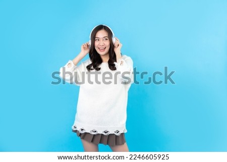 Beautiful Asian woman with long hair, casual wear, wearing white wireless headphones. Listening to music with excited emotions and happy smiles. on the blue background in the studio