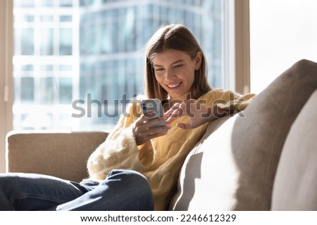 Beautiful young woman rest on sofa use mobile phone, enjoy leisure on internet, have fun use new mobile application spend time alone in sunny warm living room at home. Lifestyle, modern gadget usage Royalty-Free Stock Photo #2246612329