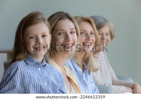 Happy beautiful cute little kid girl looking at camera, smiling, posing with young mother, mature cheerful grandma, positive great grandmother standing behind. Female generation, family portrait