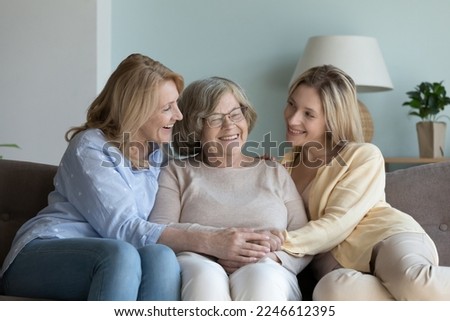 Senior mom and young adult daughter visiting elder senior grandmother, resting on sofa at home, chatting, talking, holding hands, hugging with love, care, enjoying family weekend