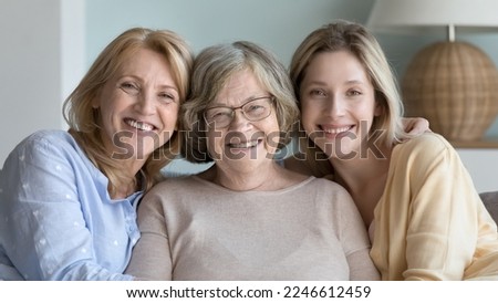 Cheerful pretty women of different ages, generations sitting close together, looking at camera, smiling, enjoying family relationships, meeting at home, leisure, mothers day