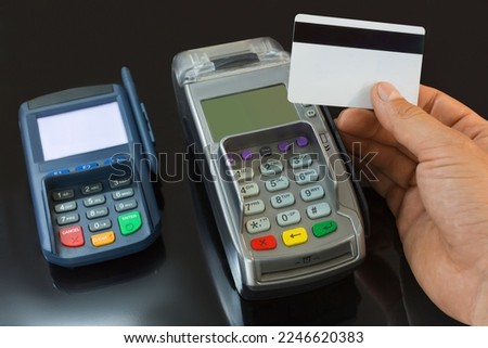 A male hand holds a payment card above the payment terminal. Close up photo.