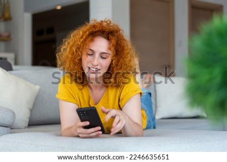 Woman using mobile phone while lying on sofa. Young female is resting at home.