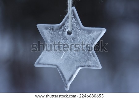Star shaped ice ornament is hanging on the tree decorating wintery garden. Things to do on a frosty day. Royalty-Free Stock Photo #2246680655