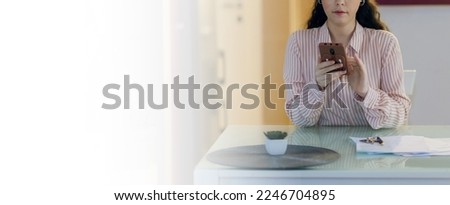 Web banner of freelance and remote work. Young beautiful Caucasian woman is sitting at table and using smartphone. Mock up. Concept of social networks and Internet search.