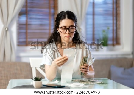 Planning of expenses. Portrait of pensive caucasian young woman accounting cash and paper receipt. Concept of payment of utilities, tax return and savings.