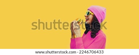 Portrait of happy cheerful young woman having fun with burger fast food isolated on yellow studio background