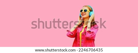 Portrait of happy smiling young woman in headphones listening to music wearing jacket on pink background