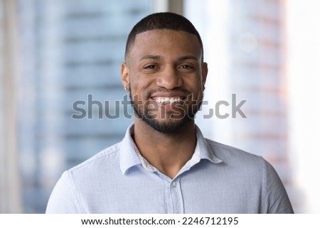African man in casual blue shirt standing indoor, smile staring at cam. Head shot of successful, ambitious businessman posing in modern office looks at camera. Professional occupation person portrait