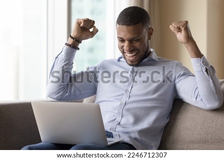 Cheerful African man read e-mail on laptop clenched fists raises his arms enjoy unbelievable commercial offer, celebrate internet lottery win, winner of on-line bet. Got hired on job of dream, luck Royalty-Free Stock Photo #2246712307