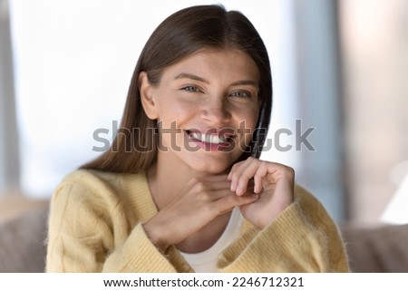 Beautiful no make-up face of young woman, close up head shot. Gorgeous millennial female sit on sofa having wide perfect white-toothed smile staring at camera, resting alone at home. Natural beauty