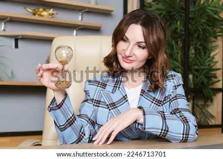 Business woman at a desk holds hourglass with shiny sand in her hands. woman looks at an hourglass as time passes. The concept of passing time.