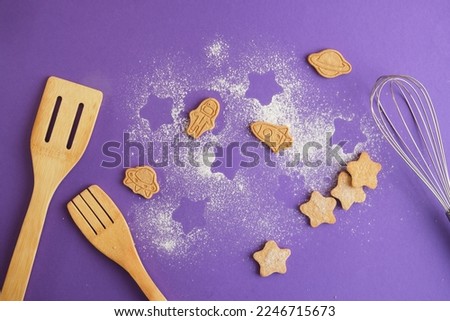 Homemade Cookiesand whisk and wooden spatula, stars and astronaut for world cosmonautics day. cookies on purple background. Space and astronomy concept