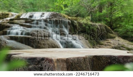 Waterfall with empty table top old wood podium outdoor in tropical forest greenery blurred background.Organic healthy natural product present placement pedestal counter display,nature jungle concept. 