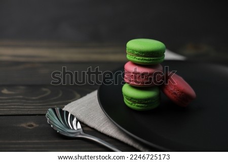 traditional American macaroons in pink and bright green color on a wooden background and a black plate next to purple fragrant flowers