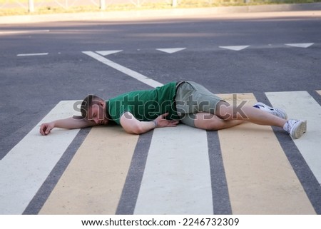 Young unconscious dead man at accident scene, crash on road, crosswalk. Pedestrian guy hit by a car on the road while crossing highway. Downed male person is lying on asphalt. Dangerous situation.  Royalty-Free Stock Photo #2246732309