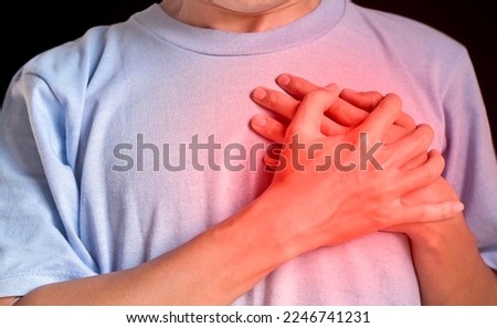 Asian young man suffering from left lateral chest pain. Chest pain can be caused by heart attack, myocardial infarct or ischemia, myocarditis, pneumonia, oesophagitis, stress, anxiety, etc,. Royalty-Free Stock Photo #2246741231