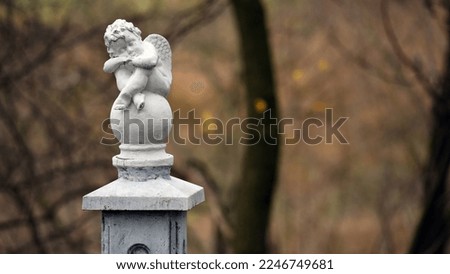 angel statue in the park. little boy with wings. cupid statue in autumn park. figurine for design, marble sad angel sitting on a ball. blurred natural background. free space for text. close-up
