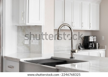A kitchen sink detail in a white kitchen with a bronze faucet, stainless steel farmhouse sink, and quartz countertops and backsplash. Royalty-Free Stock Photo #2246768325