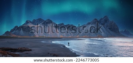 Amazing Iceland nature seascape. Iconic location for landscape photographers and bloggers. Scenic Image of Iceland. Alone tourist against Vestrahorn mountaine with Green northern lights and reflection