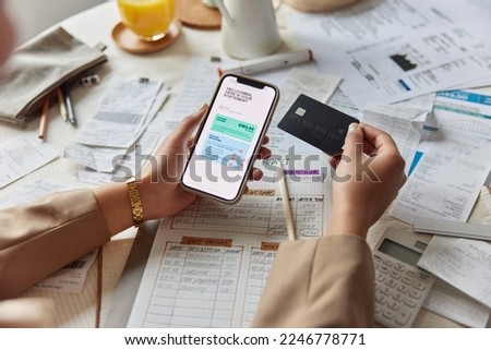 Close up shot of woman sits at table works with financial documents holds smartphone banking card manages family budget calculates expenses makes payment plans investment leads accounting of company Royalty-Free Stock Photo #2246778771