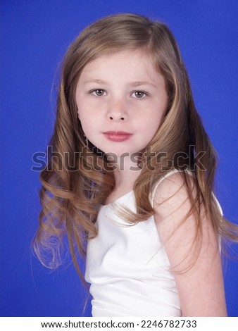 Portrait Head Shot of a Cute Young Blonde Preteen Girl Against a Blue Background