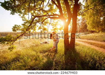 Young kissing couple under big tree with swing at sunset Royalty-Free Stock Photo #224679403